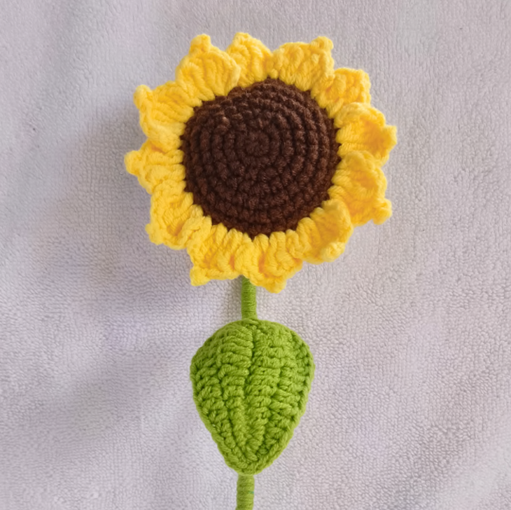 Handmade crochet sunflower amigurumi with a realistic brown center, vibrant yellow petals, and a green wired stem.