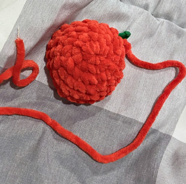 Hands crocheting a red amigurumi heart project with a 4.5 mm crochet hook, working on the upper lobes and joining stitches.