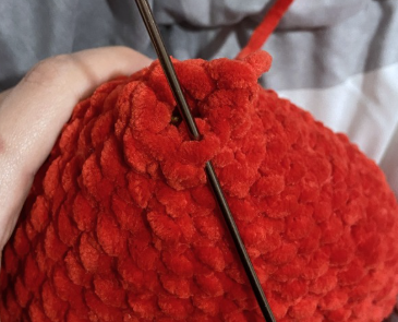 Hands crocheting a red amigurumi heart project with a 4.5 mm crochet hook, working on the upper lobes and joining stitches.
