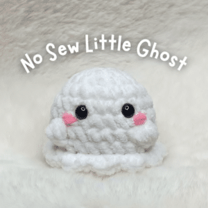 Finished handmade white crochet ghost amigurumi plush toy sitting on a fluffy white background.