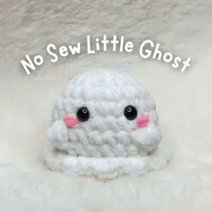 Crochet pattern cover showing a finished handmade white no-sew little ghost amigurumi with safety eyes and pink embroidered cheeks.