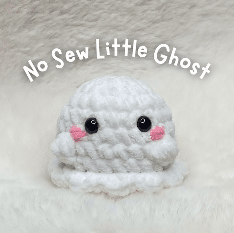 Crochet pattern cover showing a finished handmade white no-sew little ghost amigurumi with safety eyes and pink embroidered cheeks.