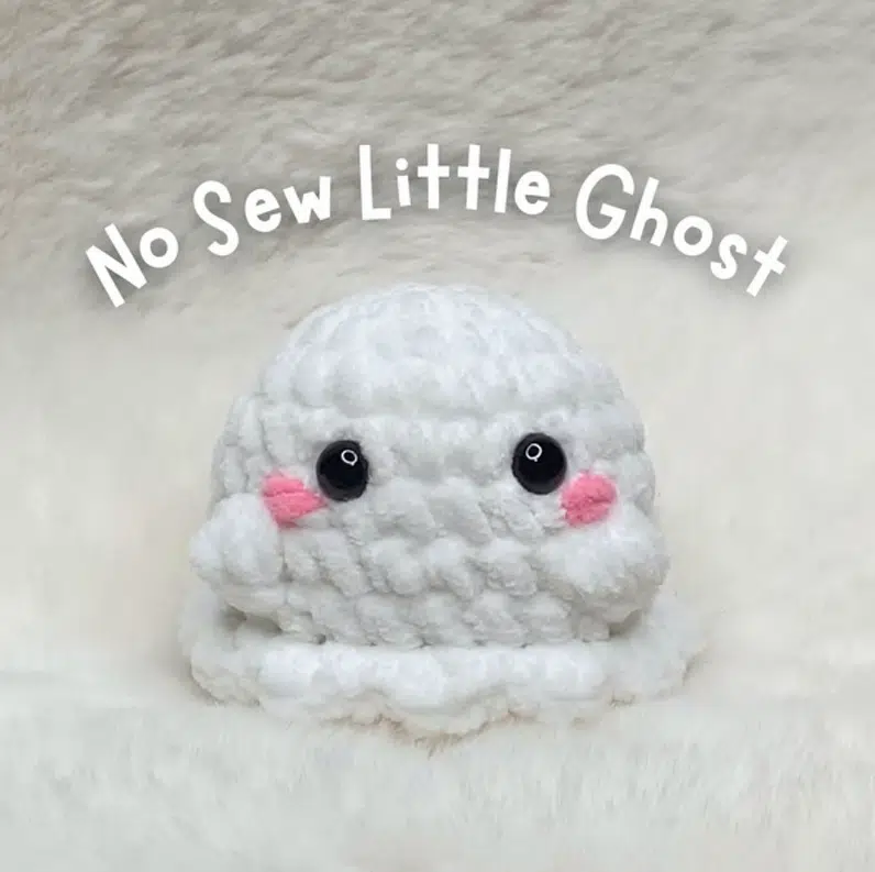 Crochet pattern cover showing a finished handmade white no-sew little ghost amigurumi with safety eyes and pink embroidered cheeks.
