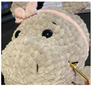 Close-up of the embroidered facial features, showing black cotton thread shaping the eyebrows and nostrils on the hippo's snout.