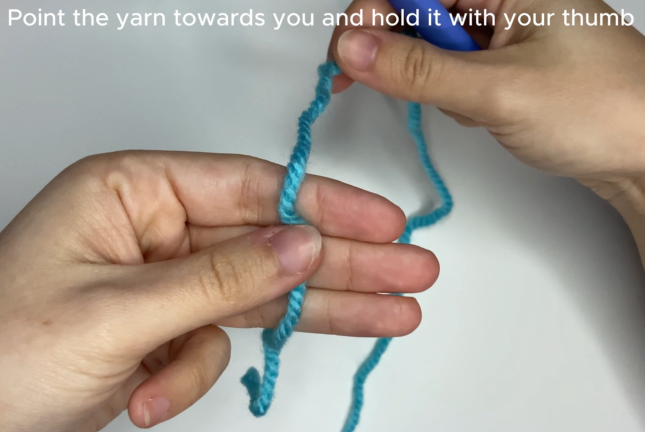 Starting a crochet magic ring: holding the yarn tail with left thumb on palm.
