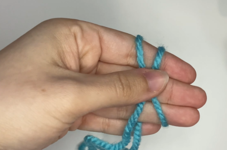 Wrapping the working yarn around left hand fingers to begin magic circle tutorial. Crossing the yarn over left fingers to create an X shape.