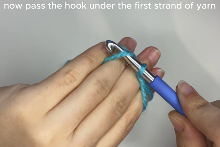 Inserting crochet hook under and over yarn strands to create a magic circle loop.