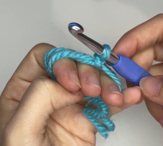 Inserting crochet hook under and over yarn strands to create a magic circle loop.