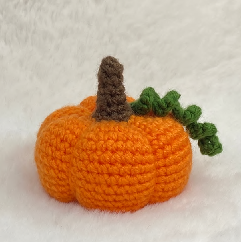 Finished handmade amigurumi little pumpkin crochet toy sitting on a white fur surface, autumn fall home decor.