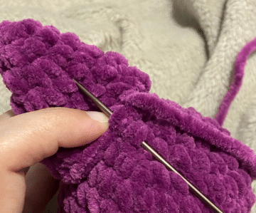 Sewing process of attaching the ears and wings to the stuffed plush bat amigurumi using a tapestry needle.