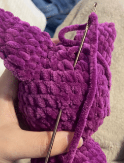 Sewing process of attaching the ears and wings to the stuffed plush bat amigurumi using a tapestry needle.