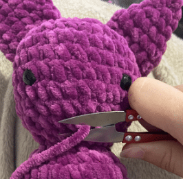 Sewing process of attaching the ears and wings to the stuffed plush bat amigurumi using a tapestry needle.