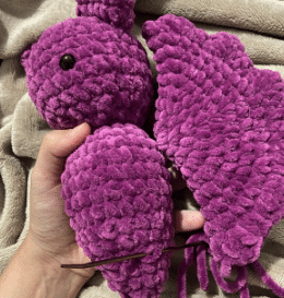 Sewing process of attaching the ears and wings to the stuffed plush bat amigurumi using a tapestry needle.