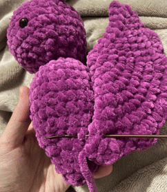 Sewing process of attaching the ears and wings to the stuffed plush bat amigurumi using a tapestry needle.