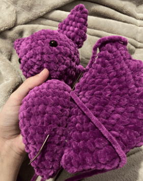 Sewing process of attaching the ears and wings to the stuffed plush bat amigurumi using a tapestry needle.