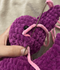 Sewing process of attaching the ears and wings to the stuffed plush bat amigurumi using a tapestry needle.