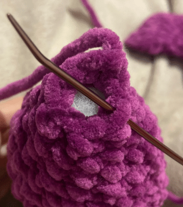 Crochet purple plush bat head and body in progress, showing stitched continuous rounds and safety eyes attached.