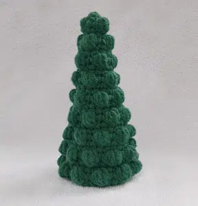 Handcrafted green bobble Christmas tree crochet amigurumi made with textured stitches against a neutral background.