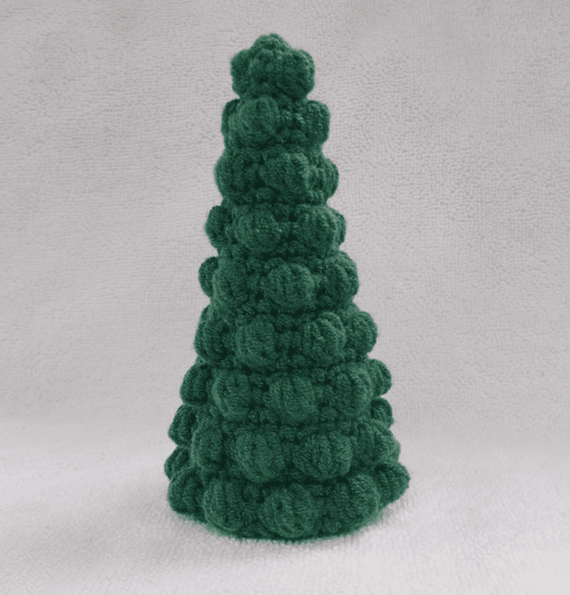 Handcrafted green bobble Christmas tree crochet amigurumi made with textured stitches against a neutral background.