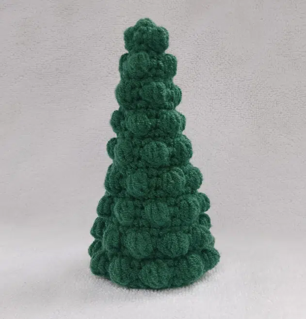 Handcrafted green bobble Christmas tree crochet amigurumi made with textured stitches against a neutral background.