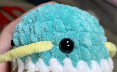 Embroidering yellow yarn beak detail on green crochet duck head using a tapestry needle between safety eyes.