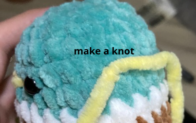 Embroidering yellow yarn beak detail on green crochet duck head using a tapestry needle between safety eyes.