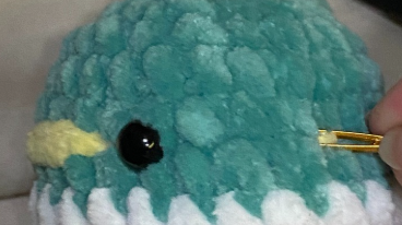 Embroidering yellow yarn beak detail on green crochet duck head using a tapestry needle between safety eyes.