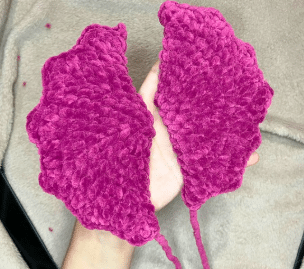 Two completed purple crochet bat wings folded in half, ready to be sewn onto the amigurumi plushie.