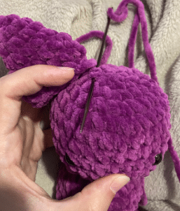 Sewing process of attaching the ears and wings to the stuffed plush bat amigurumi using a tapestry needle.