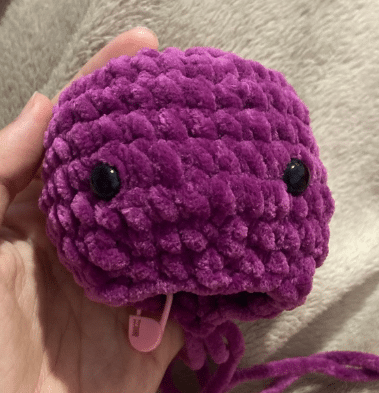Crochet purple plush bat head and body in progress, showing stitched continuous rounds and safety eyes attached.