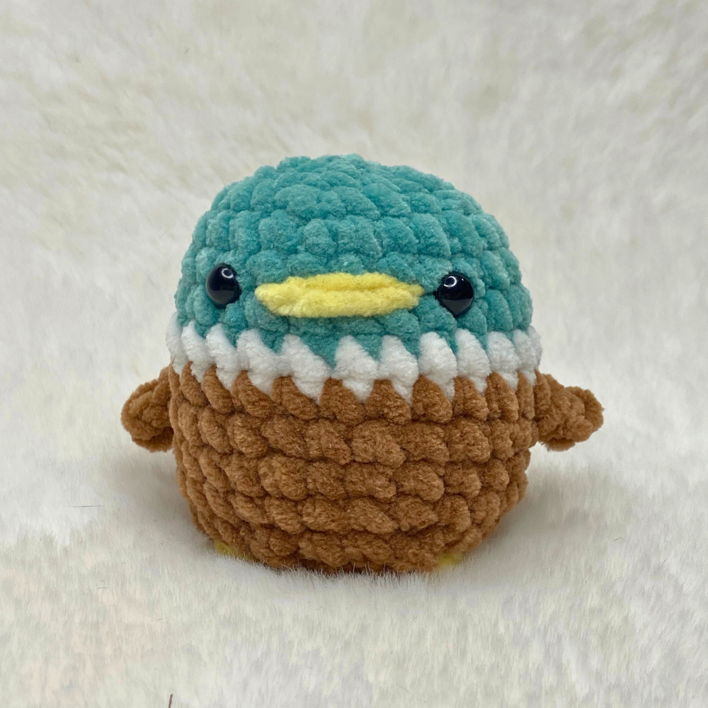 Finished plush no sew duck amigurumi made with green, white, brown, and yellow chenille yarn on a white fur.