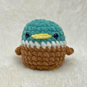 Finished plush no sew duck amigurumi made with green, white, brown, and yellow chenille yarn on a white fur background